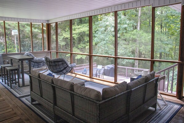 A covered outdoor seating area with wicker furniture and a view of a wooded landscape.