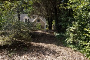 Een huis omringd door dicht bos, met een onverharde weg er naartoe.