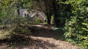 Una casa envoltada de bosc dens, amb un camí de terra que condueix a la porta principal.