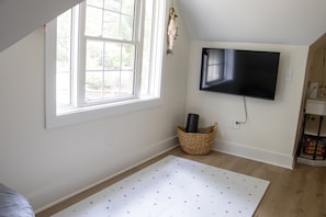A room with a large window, a flat-screen TV mounted on the wall, a woven basket, and a patterned rug on the floor.