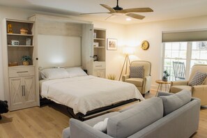 Una camera da letto con un letto, un divano, una sedia, una ventola a soffitto e una finestra.