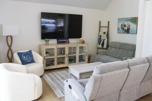 Uma sala de estar com televisão de tela plana, um armário com portas de vidro, um sofá cinza e uma poltrona branca.