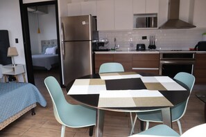 A compact hotel room with a kitchenette, a bed with a blue blanket, and a dining area with a table and chairs. - EON Zone 10: Luxury, views, and comfort all in one place. (Ciudad de Guatemala)