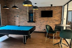 A pool table in a room with brick walls, a flat-screen TV, and modern chairs. - EON Zone 10: Luxury, views, and comfort all in one place. (Ciudad de Guatemala)
