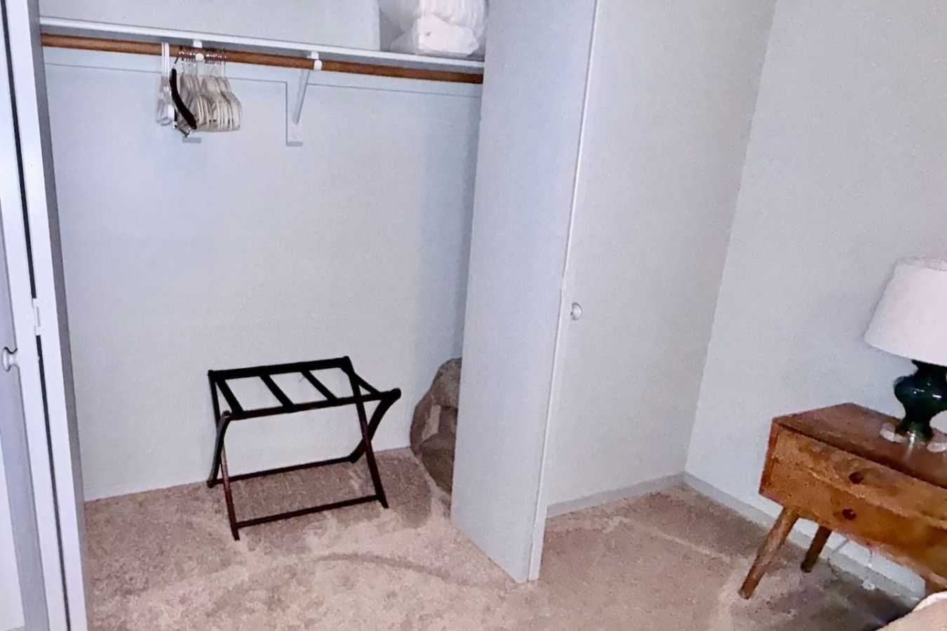 Et skab med ophængningsplads, et lille træbord og en lampe.