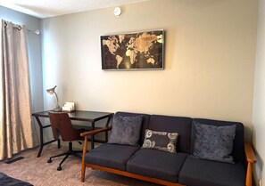 Une pièce avec un canapé sombre, une chaise en bois, une petite table et une carte du monde accrochée au mur.