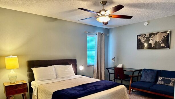 A hotel room with a bed, a desk, a chair, a globe on the wall, and a ceiling fan. - Top Stay in a Perfect Location – Crystal Bridges (Bentonville)