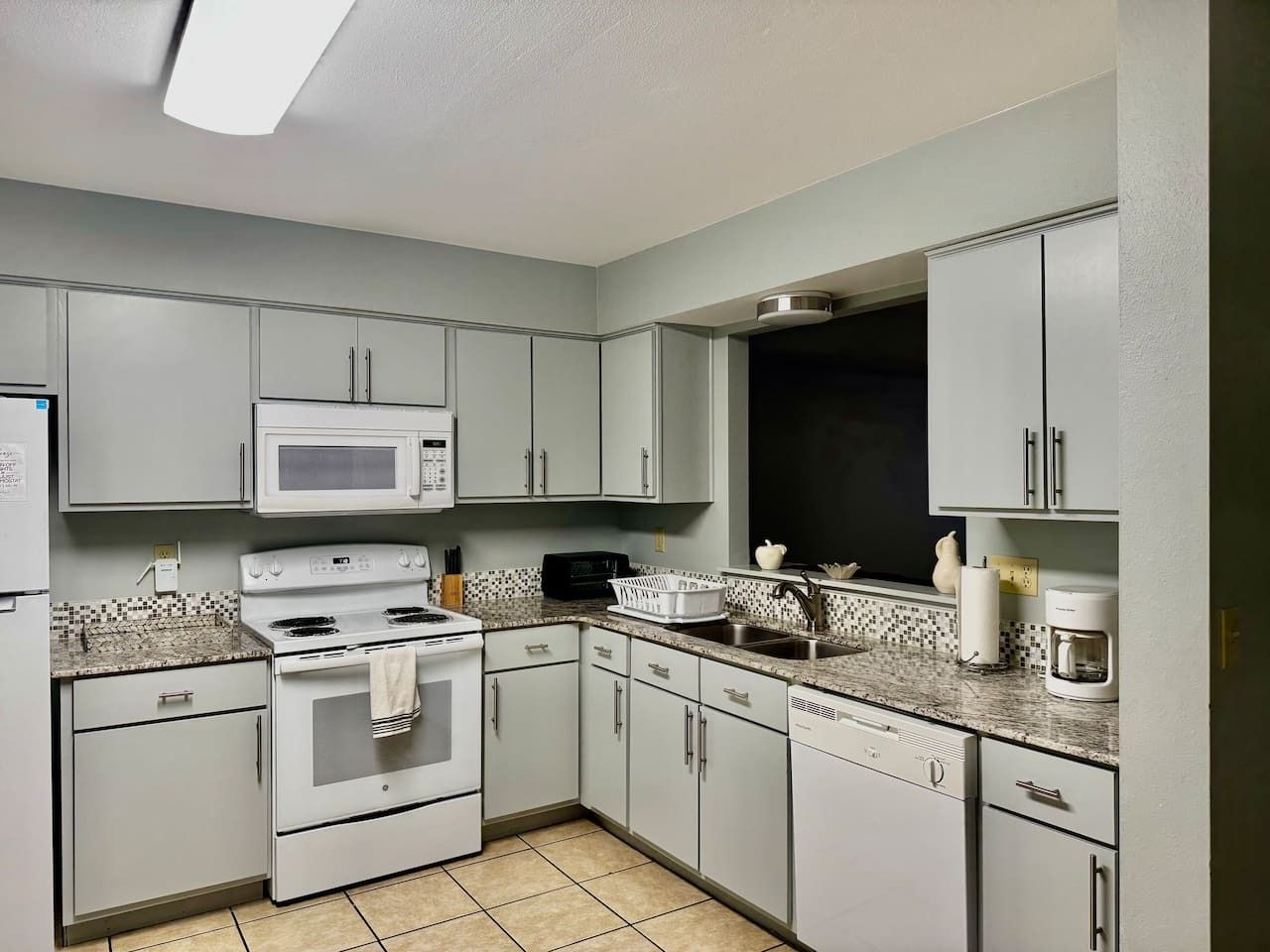A kitchen with white cabinets, a microwave, stove, and a coffee maker.