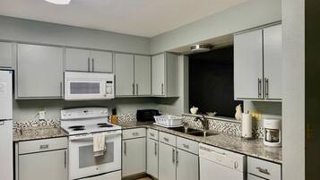 A kitchen with white cabinets, a microwave, stove, and a coffee maker.