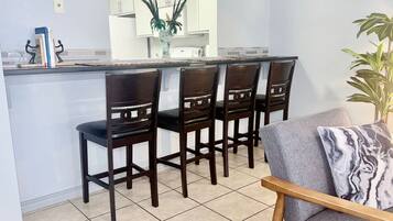 Una cocina con barra, cuatro sillas de madera, un sofá gris y una planta en maceta.