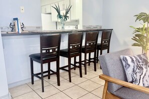 Une cuisine avec un coin bar, quatre chaises en bois, un canapé gris et une plante en pot.
