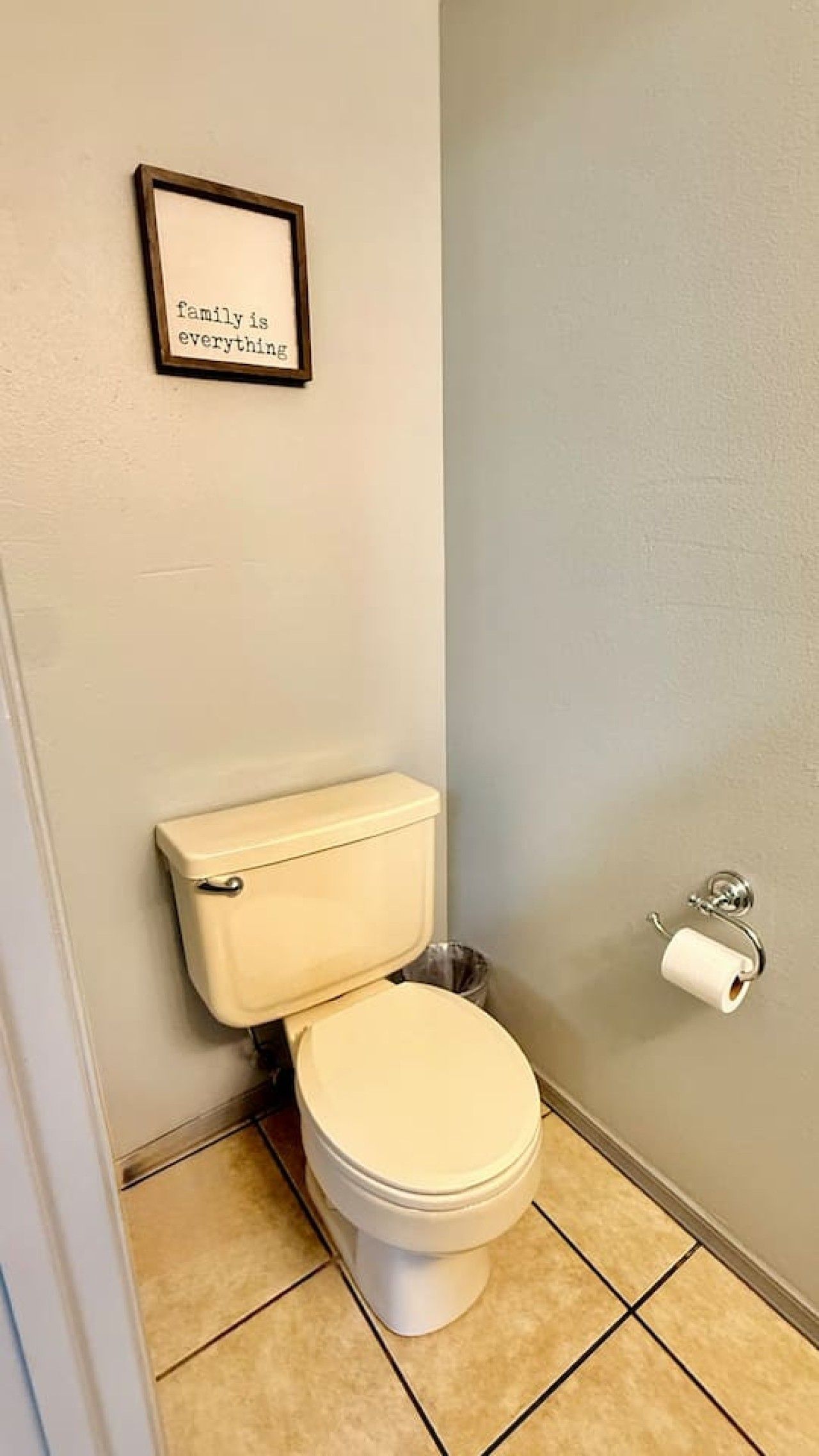 Un baño con un inodoro, una cita enmarcada en la pared y un dispensador de papel higiénico.