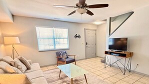 A living room with a ceiling fan, a television on a stand, a sofa, a coffee table, and a window with blinds. - Top Stay in a Perfect Location – Crystal Bridges (Bentonville)