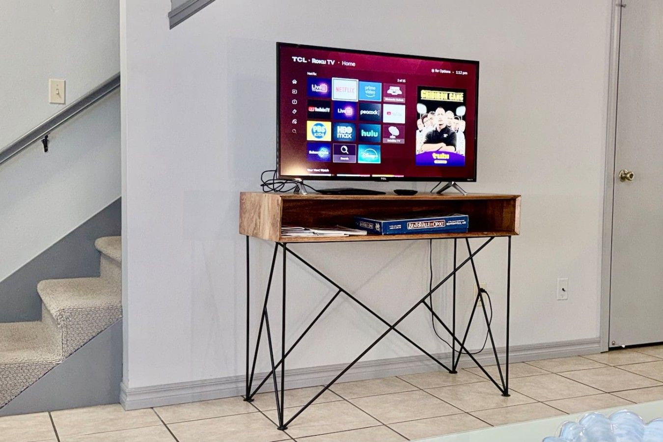 Un téléviseur posé sur un meuble en bois doté de pieds en métal, dont l’écran d’accueil affiche différents services de diffusion en continu.
