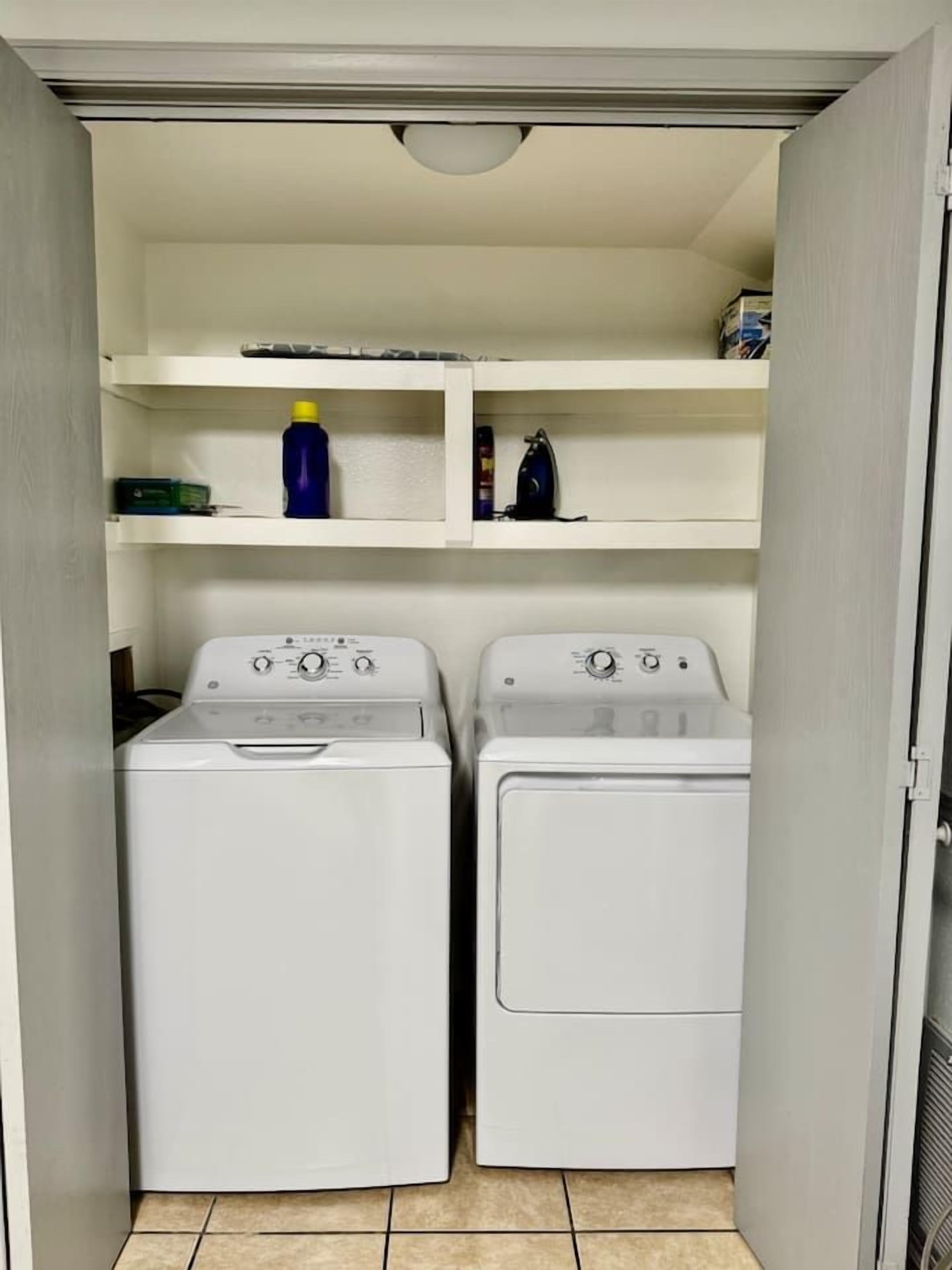 A laundry room with two white washing machines and shelves above them.