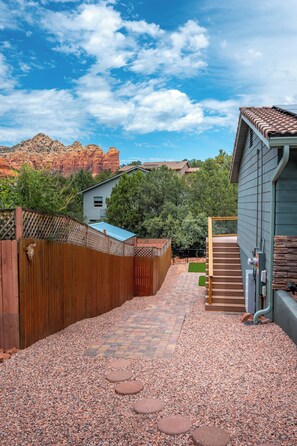 A backyard with a gravel path, wooden fence, and a house with a red-tiled roof. - Relax In Sedona/Thunder Mountain Views (Sedona)