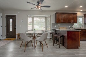 A modern kitchen with wooden cabinets, a central island, and a dining area with a glass table and chairs. - Relax In Sedona/Thunder Mountain Views (Sedona)