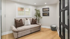 Quarto com sofá, janela com persianas, planta e quadros na parede.