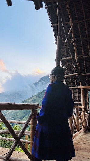 A person standing at a wooden observation deck overlooking a mountainous landscape. - Soul Nest Camp (Luhungo)