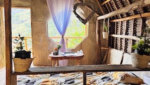 Quarto rústico com uma grande janela, uma mesinha com um vaso e uma cesta de palha.