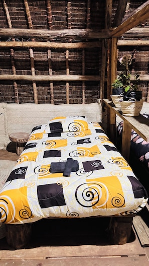 A bed with a patterned bedspread, a wooden headboard, and a rustic wall with a woven ceiling. - Soul Nest Camp (Luhungo)