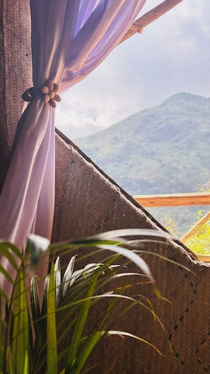 A window with a woven basket, a curtain tied with a flower, and a glimpse of a mountain view. - Soul Nest Camp (Luhungo)