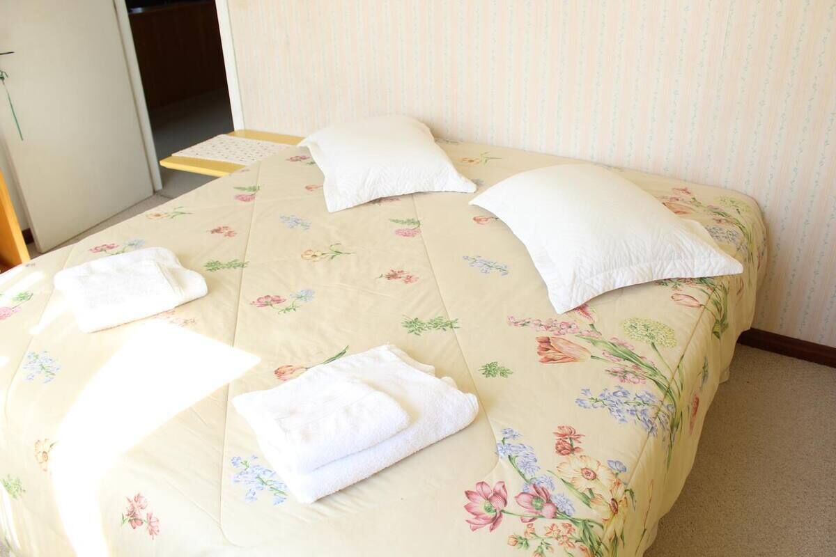 Een bed met bloemenbeddengoed, twee kussens en twee opgevouwen handdoeken.