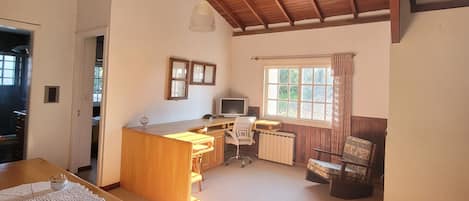 Una habitación amplia con techo de madera, una zona de cocina con mesa y silla, y un ventanal con cortinas.