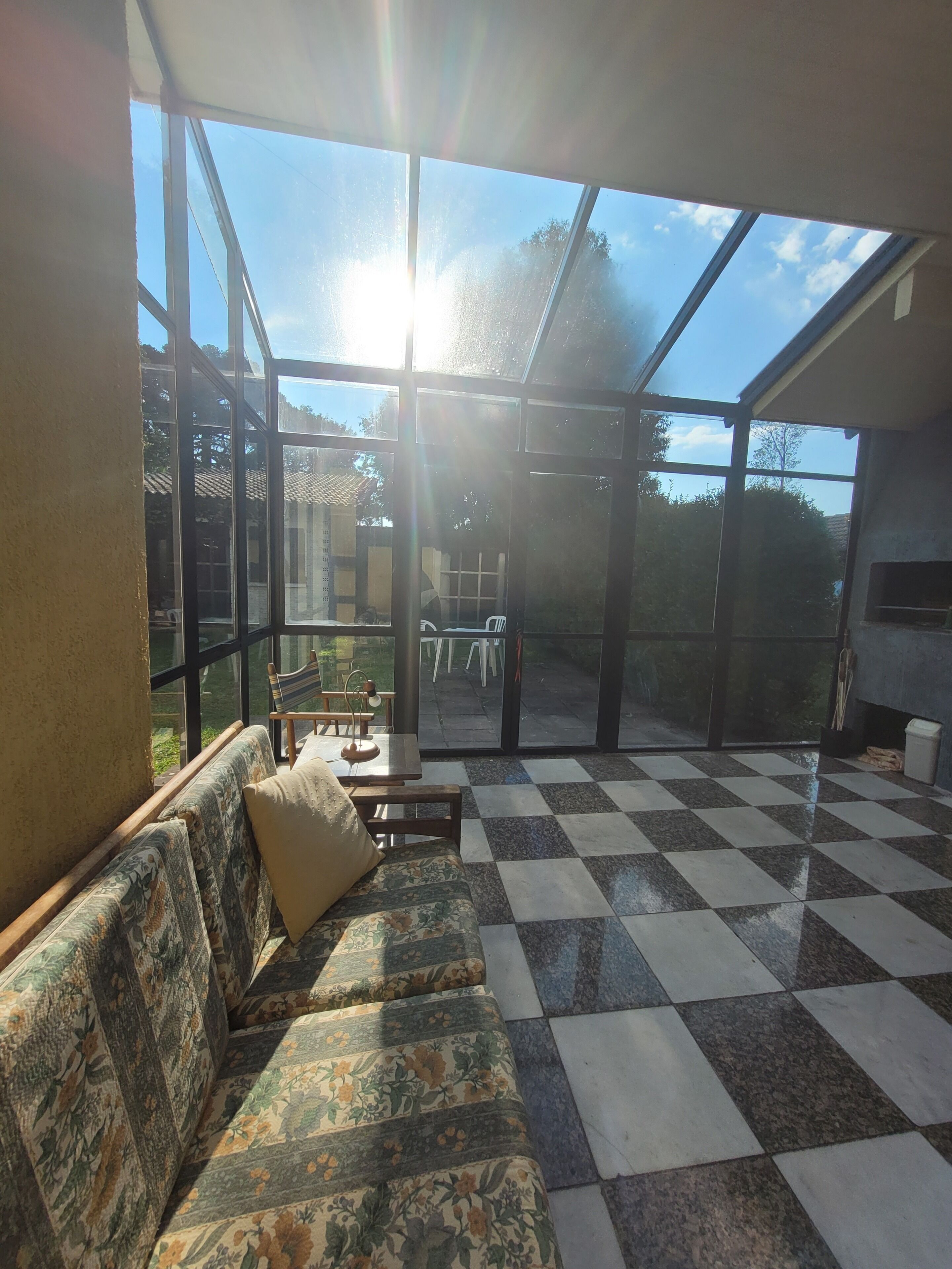 Une pièce baignée de lumière, avec un sol à carreaux, un canapé agrémenté de coussins et une vue dégagée sur l’extérieur grâce à de grandes fenêtres.