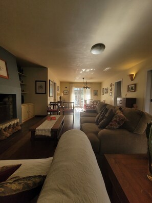 A spacious living room with a fireplace, a sofa, a dining area, and a view of the outdoors.