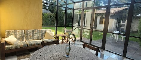 A conservatory with a checkered floor, a round table with a lace tablecloth, and a sofa with cushions.