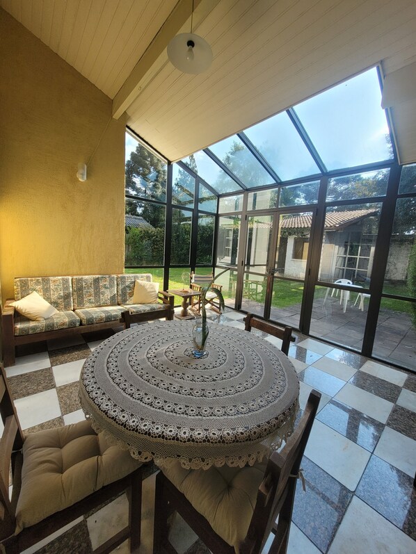 A conservatory with a checkered floor, a round table with a lace tablecloth, and a sofa with cushions.