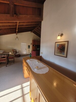 A dining area with a wooden table, chairs, a kitchen in the background, and a ceiling with exposed beams.