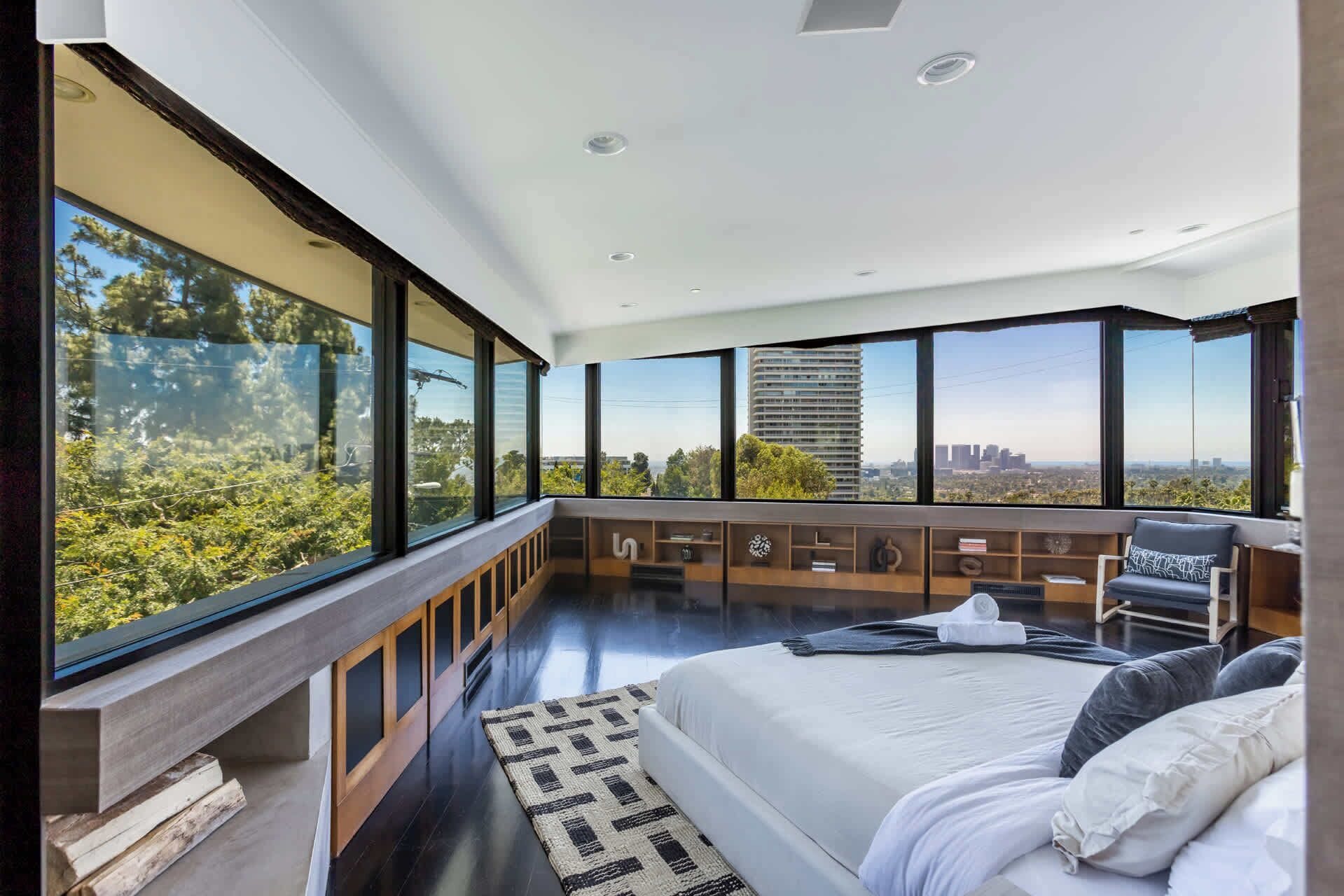 A modern bedroom with a large bed, a seating area, and a view of the city.