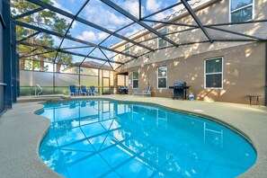 Une piscine intérieure à l’eau d’un bleu cristallin, entourée de chaises longues et d’un barbecue.