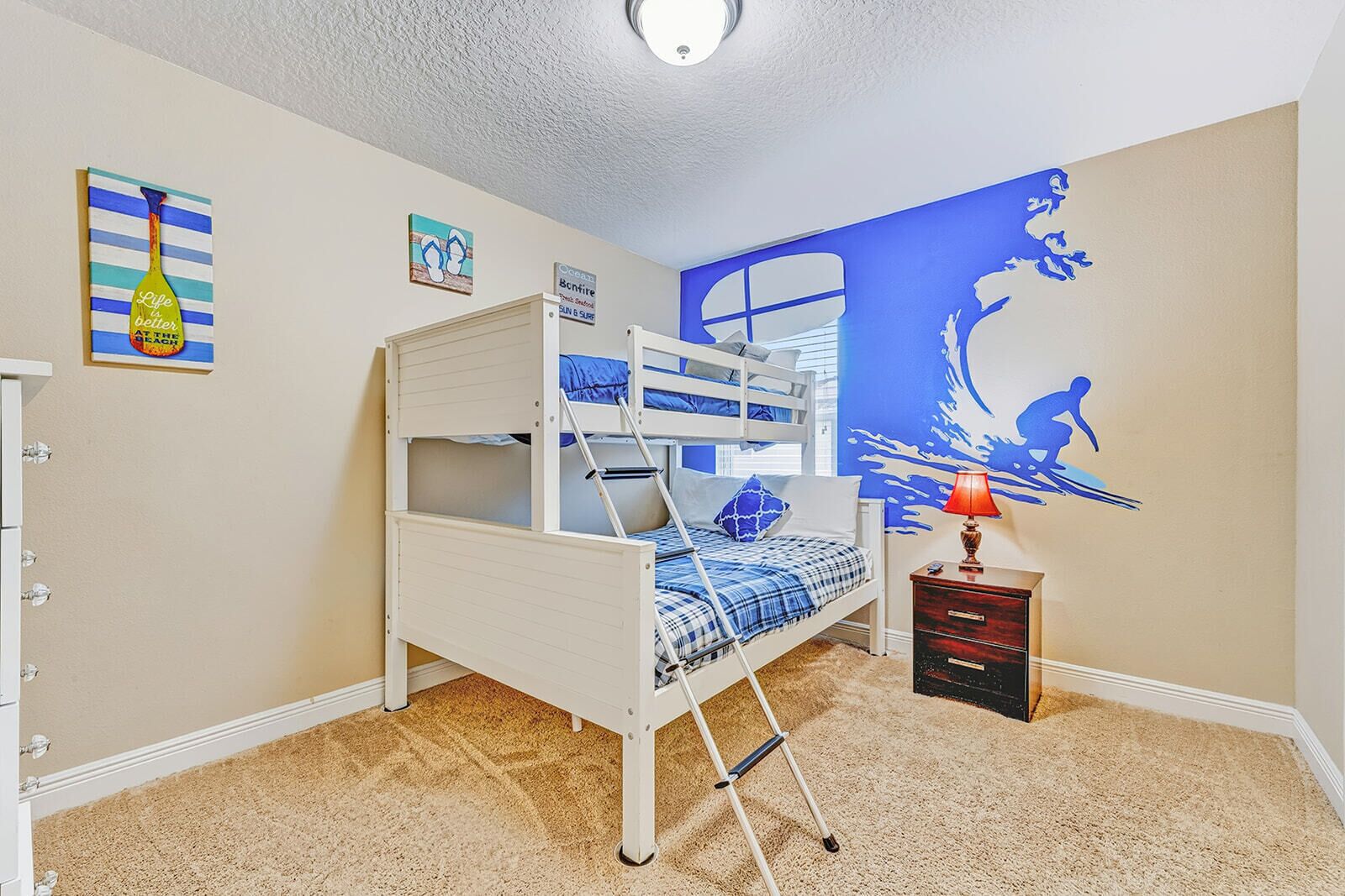 A bunk bed room with a blue ocean mural, a small desk with a lamp, and a dresser.