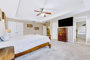 Une chambre à coucher avec un lit, une commode, un ventilateur de plafond et un téléviseur.