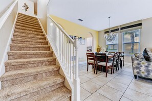 A staircase leading to a dining area with a chandelier, a dining table with chairs, and a patterned sofa. - Orlando Escape! Pool-Spa-Theater-GameRoom:4-15 PPL (Davenport)