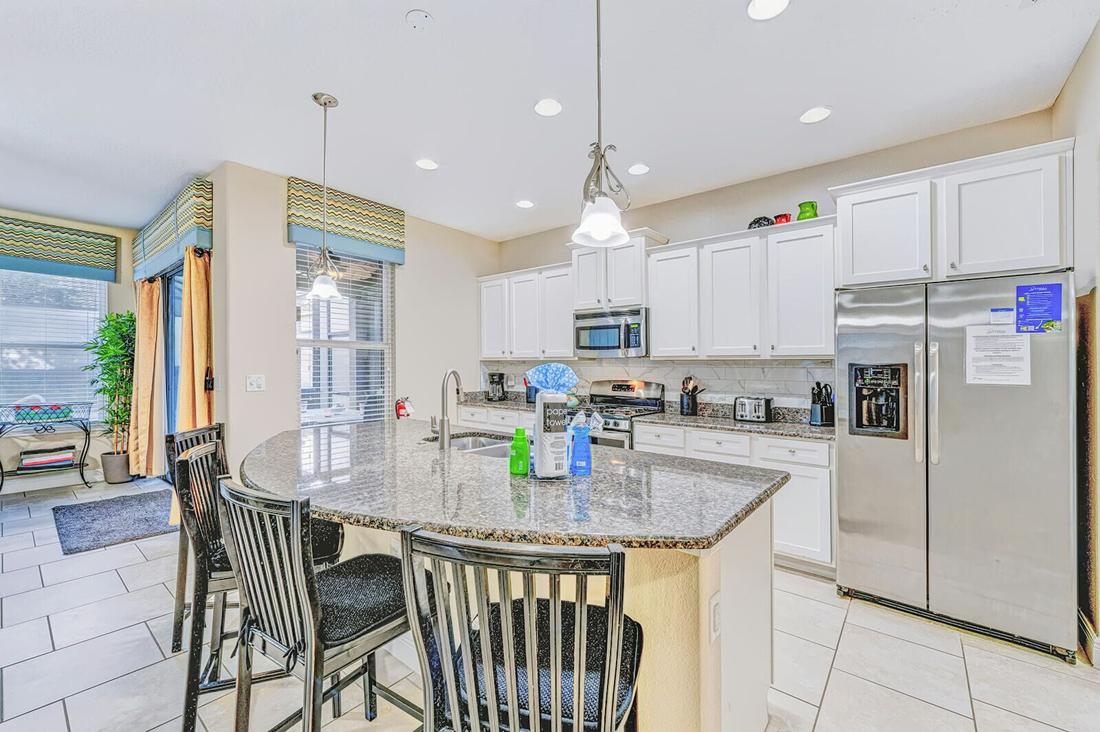 A modern kitchen with a central island, stainless steel appliances, and a dining area with chairs.