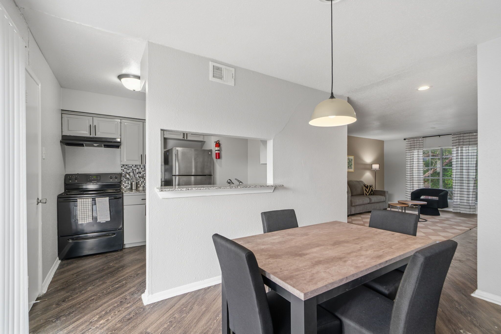 A modern kitchen with a built-in oven and refrigerator, a dining area with a table and chairs, and a living room with a sofa and a window.