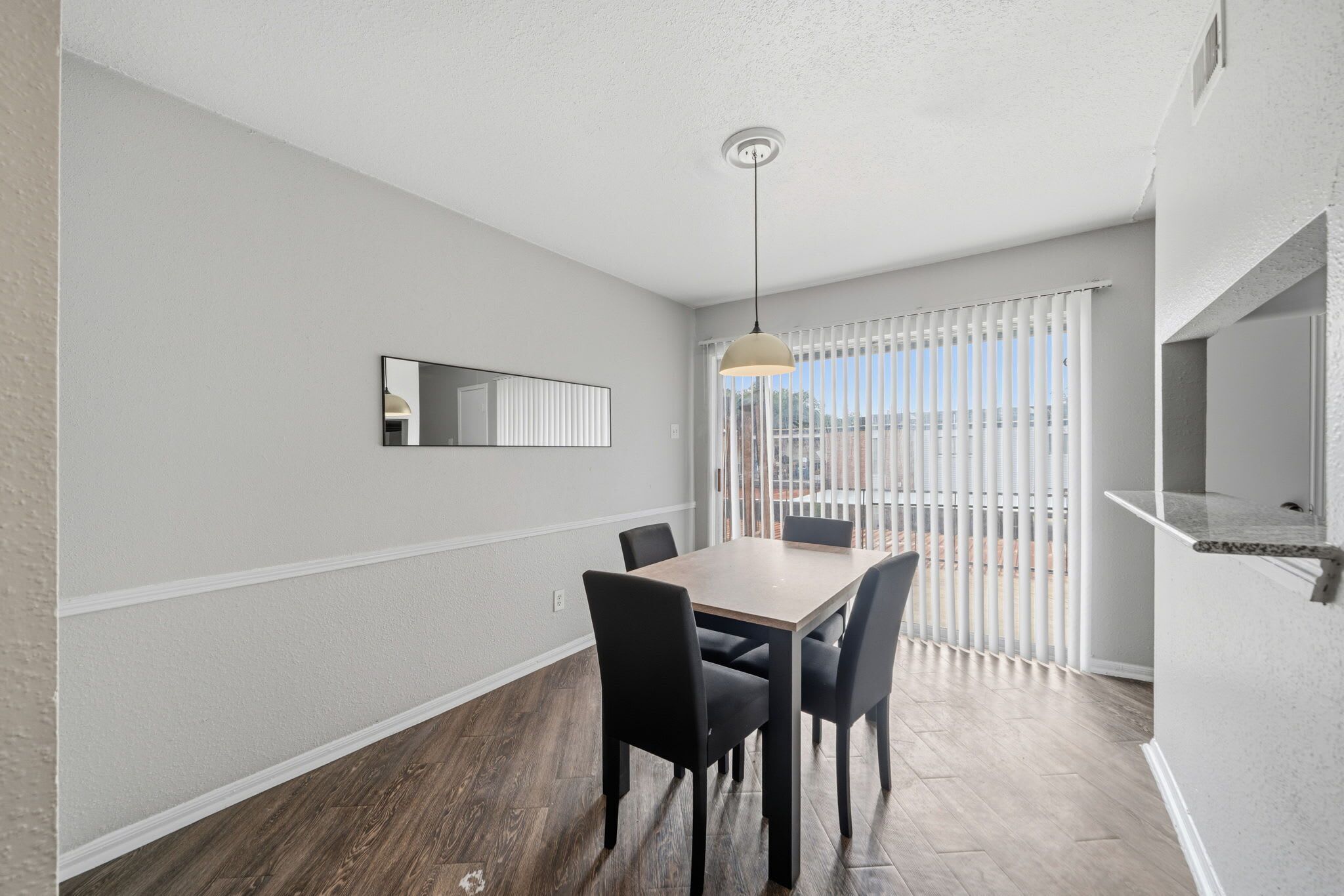 A dining area with a table and chairs, a hanging light fixture, and a window with blinds.
