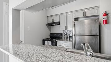 A kitchen with white cabinets, a stainless steel refrigerator, a stove, and a fire extinguisher.