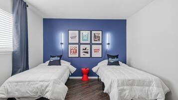 Une chambre avec deux lits, un tabouret rouge et des œuvres d’art murales.