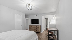 Ein Schlafzimmer mit Bett, Kommode, Fernseher und Schreibtisch mit Stuhl.