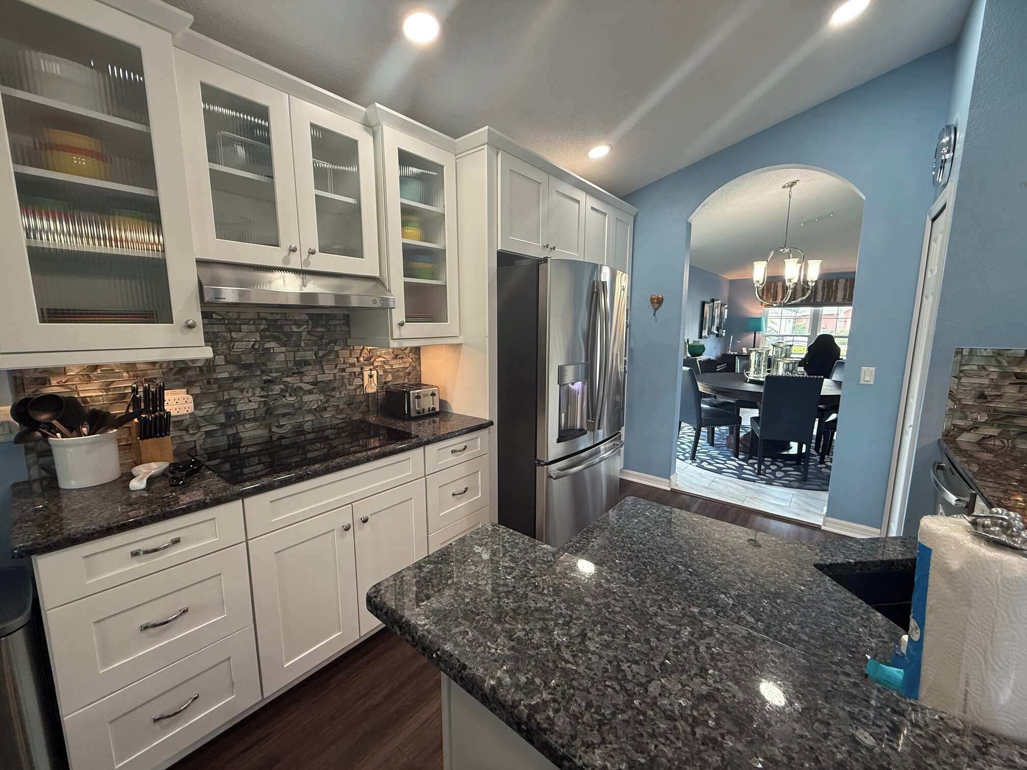 A modern kitchen with white cabinetry, granite countertops, and a stainless steel refrigerator.