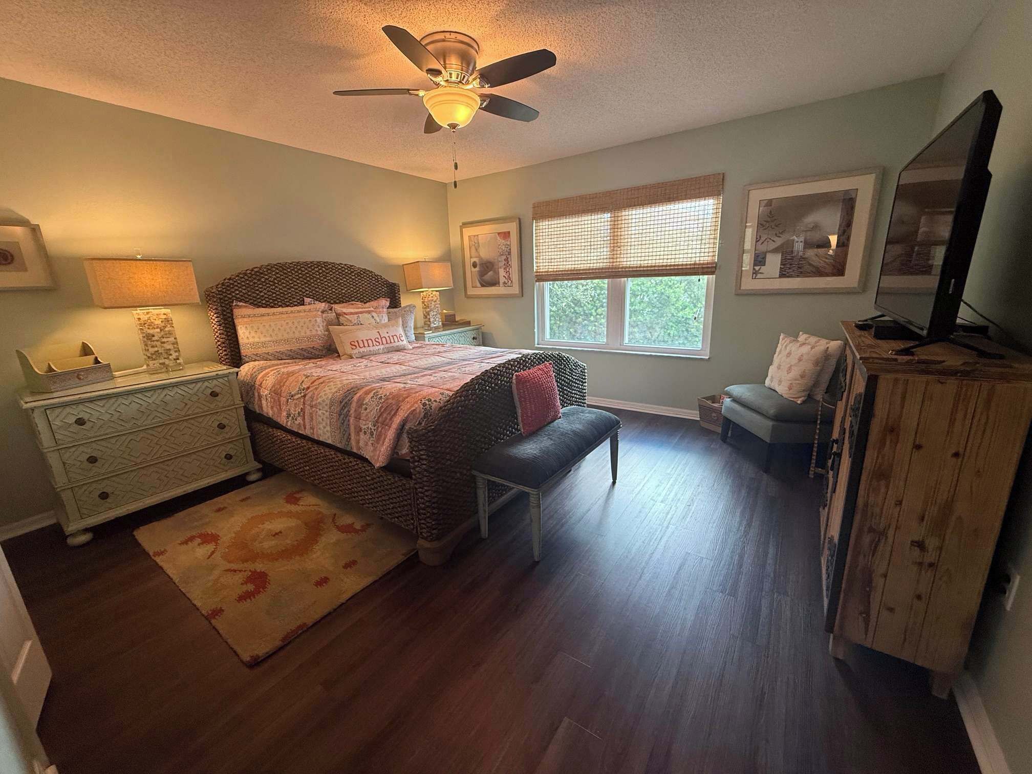 A bedroom with a bed, bedside tables, a bench, a window with blinds, and a ceiling fan.