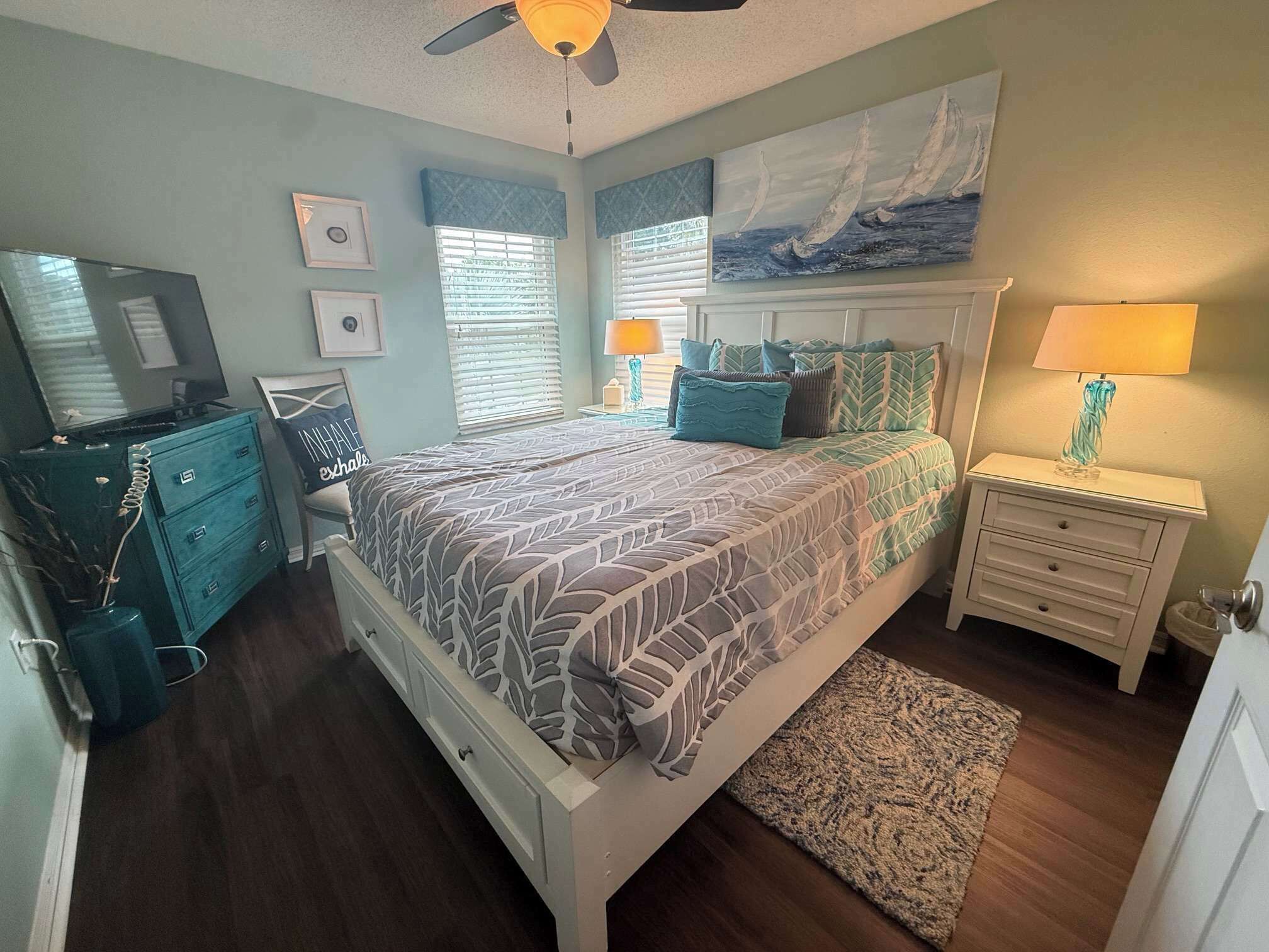 A bedroom with a bed, a dresser, a nightstand, a lamp, and a painting on the wall.