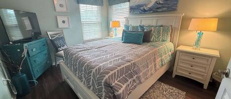 A bedroom with a bed, a dresser, a nightstand, a lamp, and a painting on the wall.