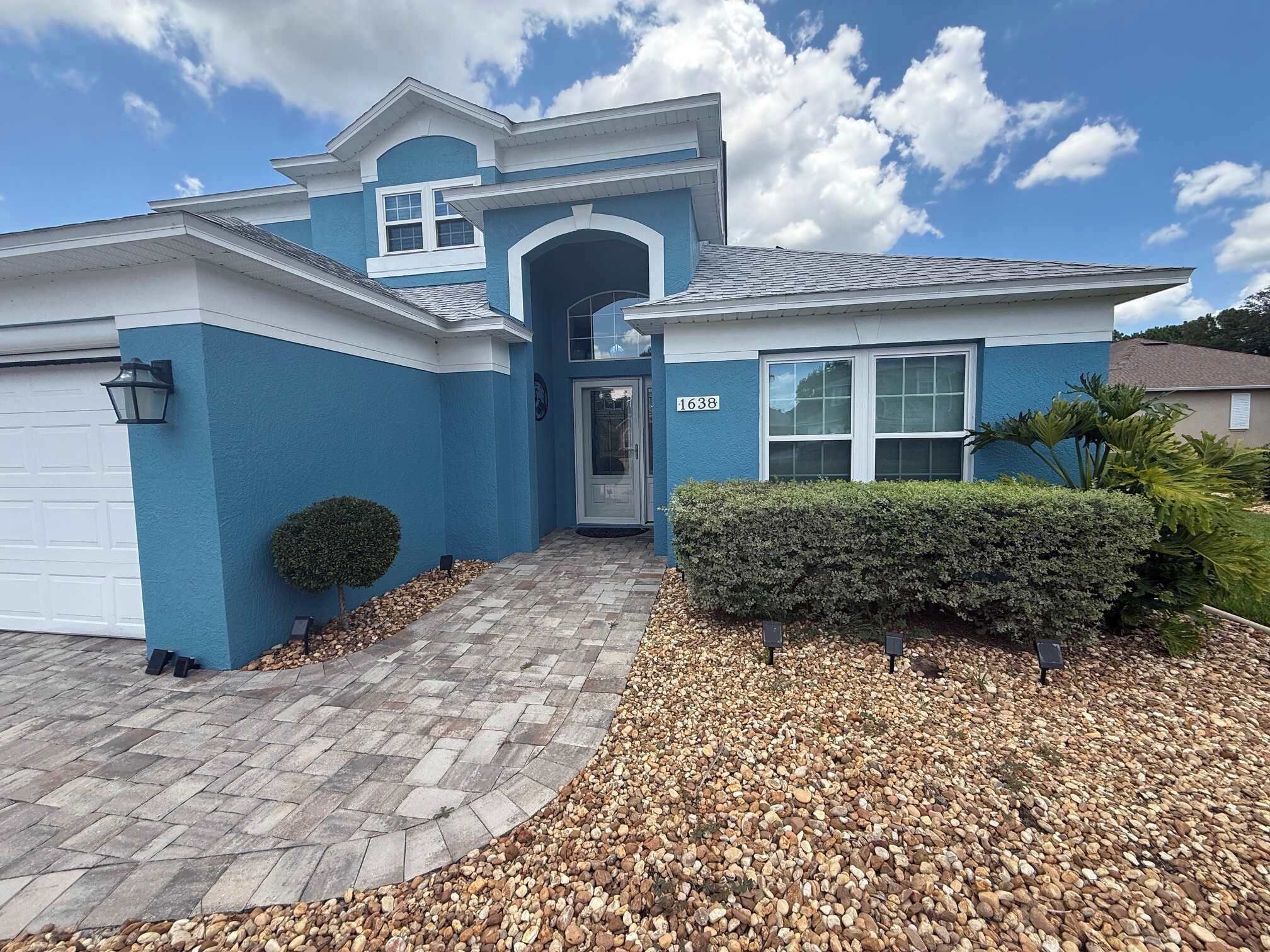 A residential house with a blue exterior, a garage, a front door, and a driveway leading to the entrance.