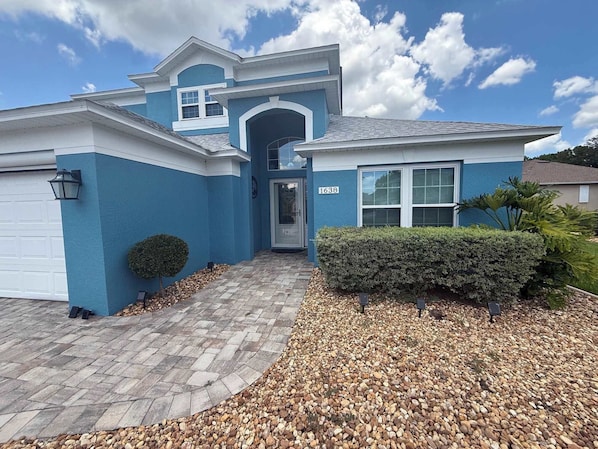 A residential house with a blue exterior, a garage, a front door, and a driveway leading to the entrance. - Peaceful Backyard Paradise (Haines City)